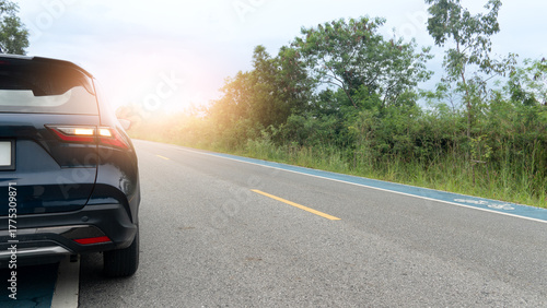 Rear side of dark luxury car with turn on right signal on the asphalt road. Turn on the signal to request to drive in the normal lane. With bicycle lane and side of raod with green grass and trees.