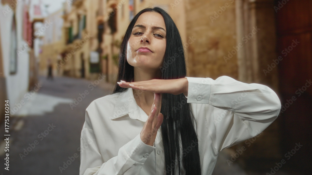 Naklejka premium Young hispanic woman making time-out gesture on old town street outdoors wearing white shirt with ancient buildings blurred in background capturing cultural essence and urban charm