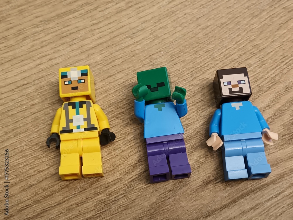 Naklejka premium Three distinct Lego Minecraft minifigures Steve, a Zombie, and another character, stand on a wooden surface, highlighting the video game's transition into physical collectible toys