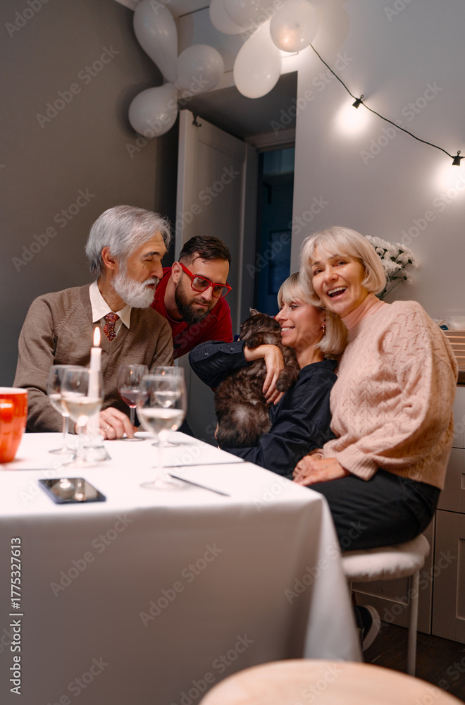 Naklejka premium A cozy gathering of family and friends enjoying each other's company indoors, sharing warm moments with a beloved pet cat. Decor and cheerful ambiance enhance the special occasion.