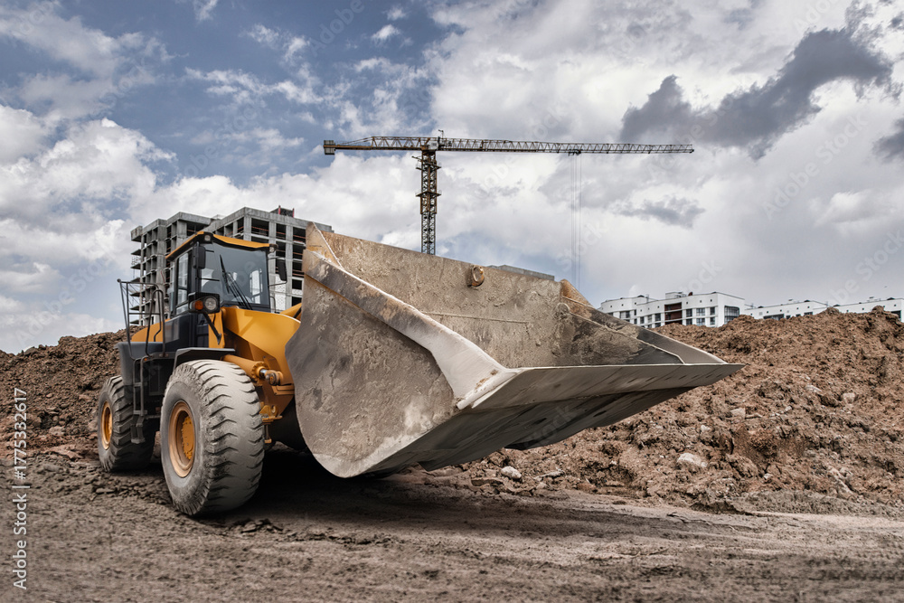 Fototapeta premium A powerful loader digs into the ground at a construction site, preparing for new buildings under a dramatic sky filled with clouds