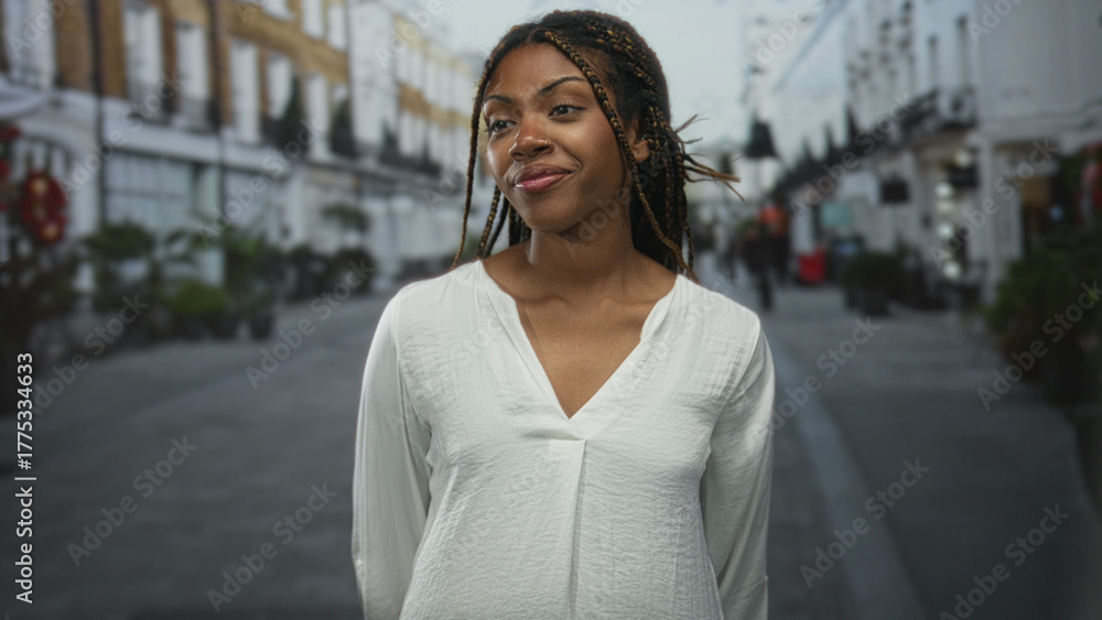 Fototapeta premium Woman smiling with braided hair and nose ring standing on a city street in front of shops wearing white blouse and relaxed posture; confidence.