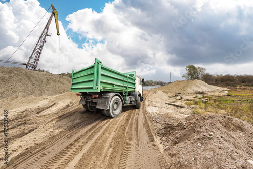 Fotografie A sturdy green truck moves along a rugged dirt path beside a construction area,