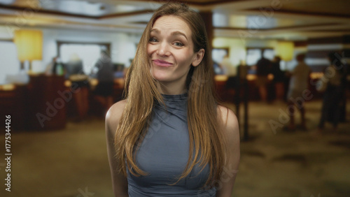 Photos Young caucasian woman makes money gesture by pinching fingertips in hotel building lobby with a skeptical smile; greed
