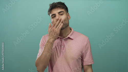 Foto Man in pink polo shirt gently blows a kiss with hand extended in a turquoise studio setting; affection