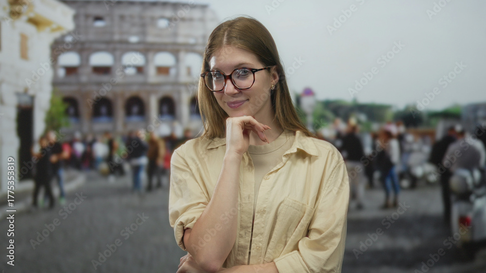 Fototapeta premium Young blonde woman wearing glasses in beige shirt touches chin with hand in street by coliseum; curiosity.
