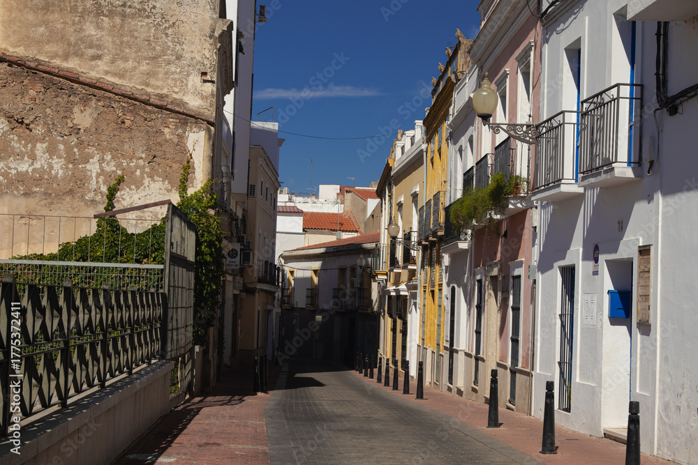 Naklejka premium Calle tradicional y estrecha en el centro histórico de Mérida, Extremadura, España, con fachadas antiguas, balcones y bolardos.