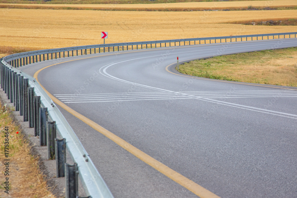 Fototapeta premium Curve in the road surrounded by golden fields on a clear day