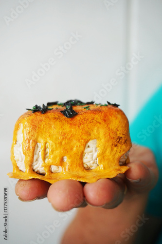 a hand holding 1 on 1 replica of japanese onigiri topped with mentai sauce and seaweed on wooden background