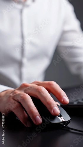 Close-up of a hand using a black computer mouse, against blurred shirt and surface