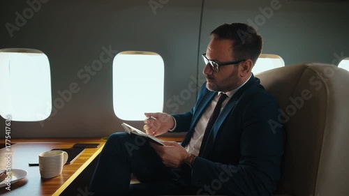 Focused mature businessman with glasses writing in his notebook while traveling in a luxurious private jet, preparing for a business meeting during an international first-class flight