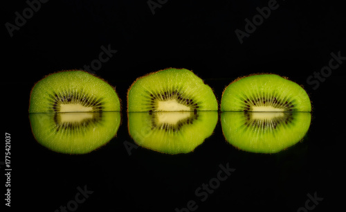 Three kiwi slices with mirroring and black background. 