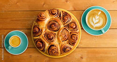 Homemade cinnamon rolls from yeast dough and two cups of coffee cappuccino and espresso on wooden table. Top view.