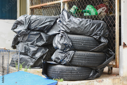 Stacked tires covered in black plastic near a chain-link fence.