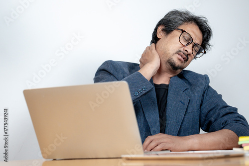 A man sitting at his desk, holding his neck and shoulder in pain due to long hours of computer work. Concept of office syndrome.
