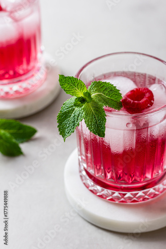 Raspberry drink with ice in a glass on a light background