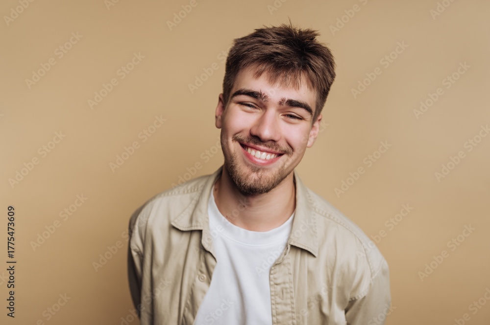 Obraz premium Smiling young man with a beard against a beige background.