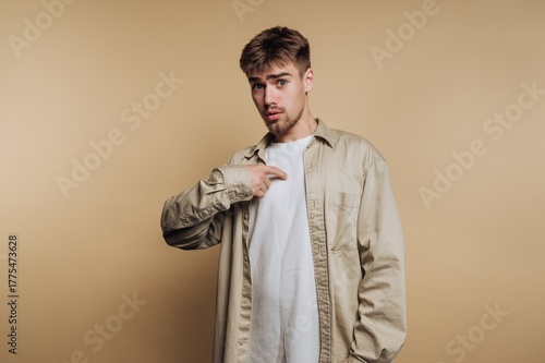Tableau sur toile Young man in casual clothing pointing at himself against a beige background
