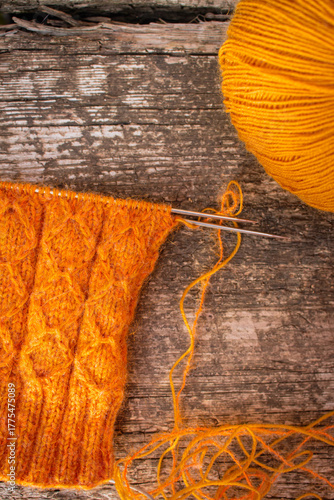 Cozy knitted socks with yarn ball and knitting needles. Orange wool socks on wooden background. Cozy autumn colours. Knitting pattern close up. Knitting hobby. Knitwear concept. Needlework background.