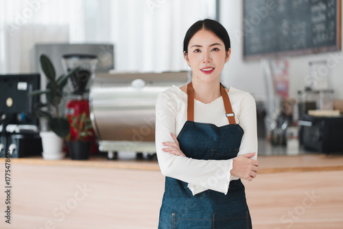 Confident smiling young Asian woman owner of small business cafe. proud entrepreneur and barista standing with arms crossed in her shop