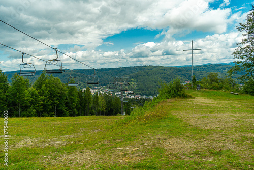 Large metal cross on Krzyzowa Mountain in Krynica Zdroj, Poland, overlooking the town and chairlift on a cloudy day.