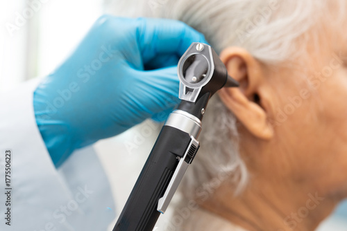 Audiologist or ENT doctor use otoscope checking ear of asian senior woman patient treating hearing loss problem.