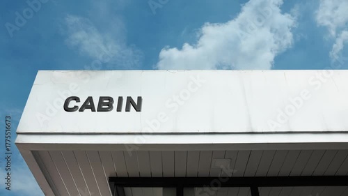 Cabin word sign simply displayed on the rustic, wooden exterior of a small dwelling beneath a clear blue sky, signifying a cozy, secluded, often wilderness-based residential or recreational retreat