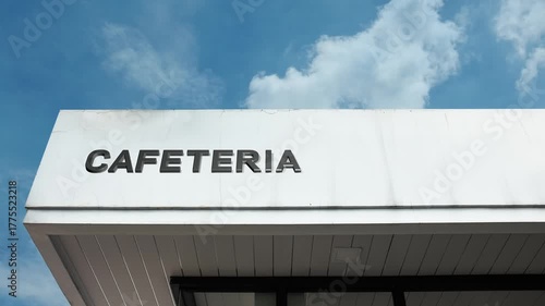 Cafeteria word sign clearly displayed on the exterior of a commercial or institutional building beneath a bright blue sky, signifying a self-service restaurant for meals and casual dining