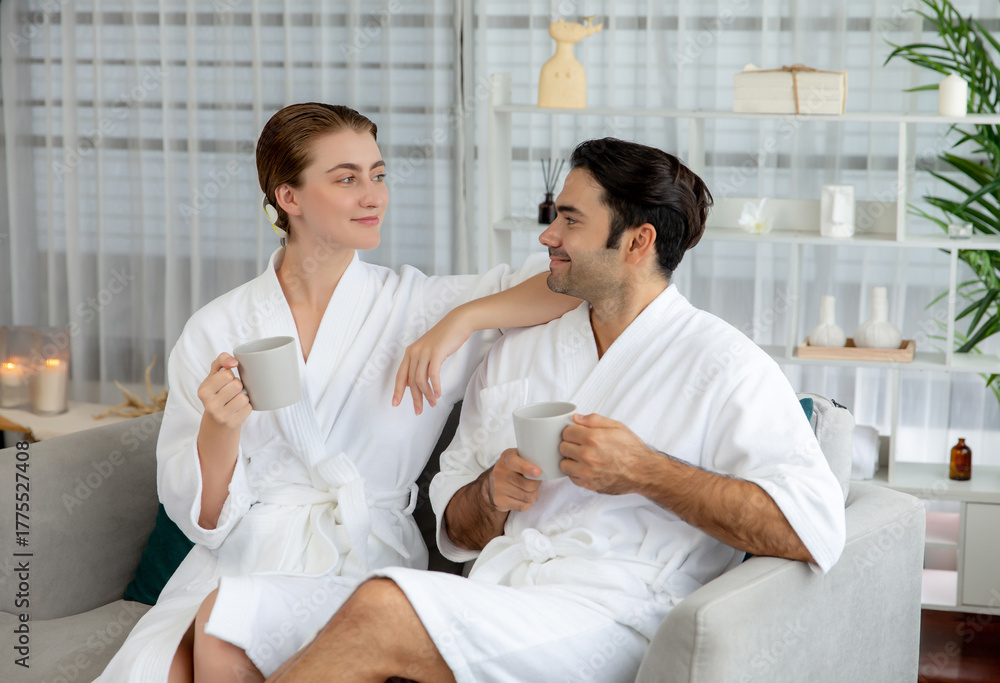 Fototapeta premium Beauty or body treatment spa salon vacation lifestyle concept with couple wearing bathrobe relaxing with drinks in luxurious hotel spa or resort room. Vacation and leisure relaxation. Quiescent