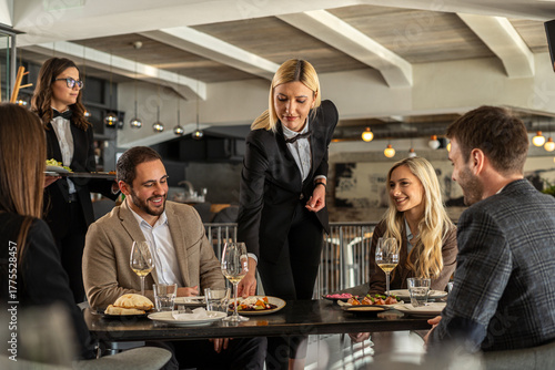 Elegant restaurant scene with server serving food to happy customers at a table