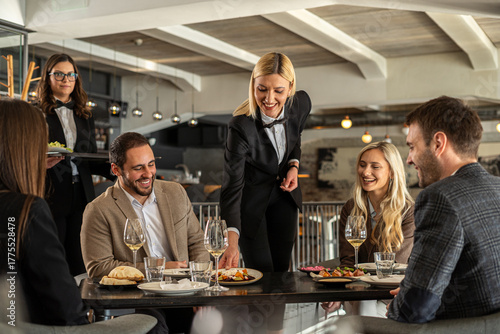 Restaurant staff serving food to a group of happy customers at a table
