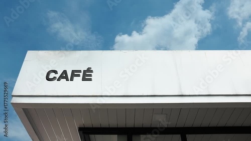 Café word sign invitingly displayed on the commercial facade of a small building beneath a clear blue sky, signifying a casual, social establishment for coffee, light meals, and conversation