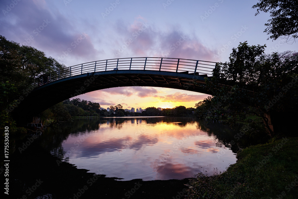 Naklejka premium A still image of the iron bridge over the lake in Ibirapuera Park, Sao Paulo, with the sunset.