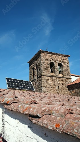The juxtaposition of an ancient stone bell tower of a historic church and a sleek solar panel on a worn rooftop captures the harmonious mix of tradition and sustainable technology