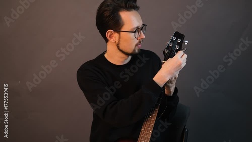 Portrait of a young male musician inserting a string into a guitar

