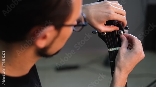 Portrait of a young male musician inserting a string into a guitar

