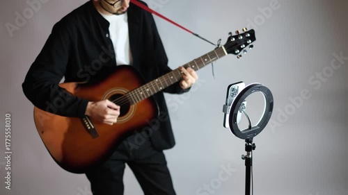 Portrait of a young guitarist recording a video of himself playing guitar for social media

