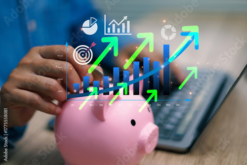 Hand putting coin into piggy bank with digital financial graph, showing profit growth, business analytics, and investment target future success concept modern technology finance