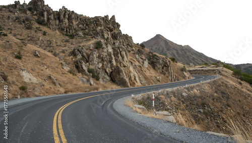 Curved asphalt road with yellow lines passes by rugged rocky cliffs and dry vegetation on a mountain slope png