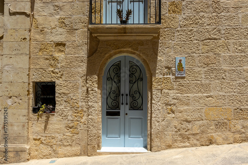 A typical house front in Birgu, Malta - with white doors and balcony and a St. George plaque (translation: St. George)