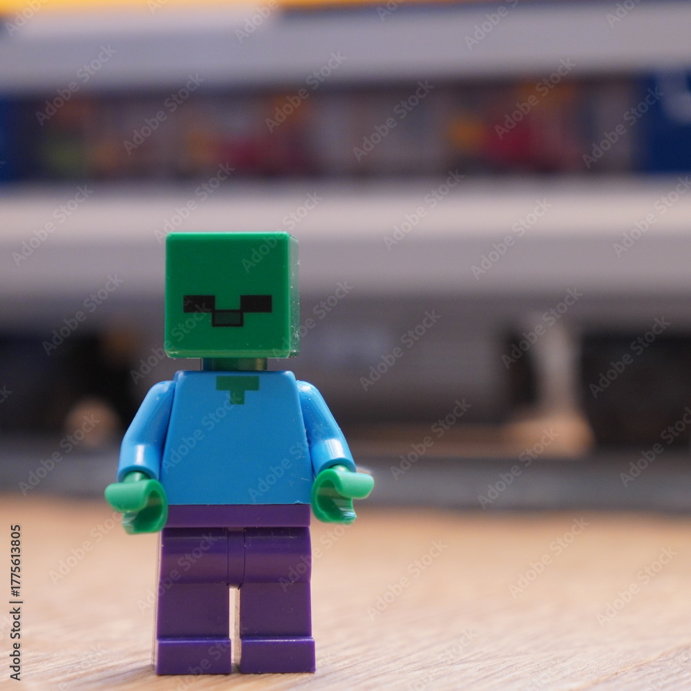 Naklejka premium A close-up photograph of a LEGO Minecraft Zombie minifigure, a popular character from the sandbox video game, standing on a wooden surface. EDITORIAL USE ONLY