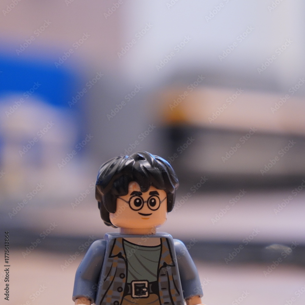 Naklejka premium Close-up of a Lego Harry Potter minifigure with his signature round glasses and black hair, standing in a room with a blurred background