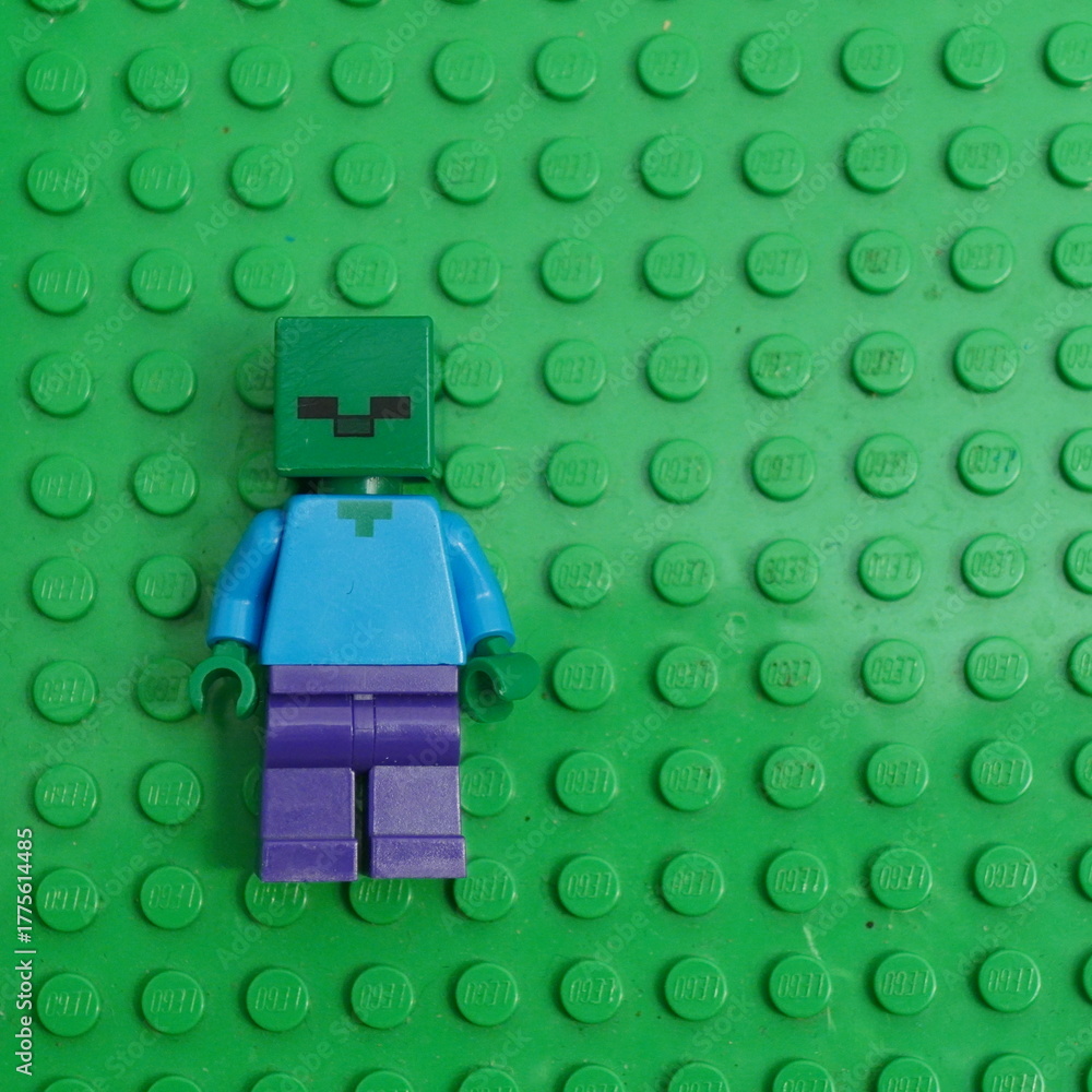 Fototapeta premium A Lego Minecraft Zombie minifigure, a popular character from the video game, stands on a green Lego baseplate
