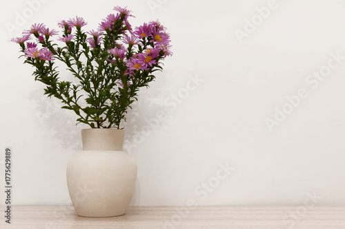 There are lilac flowers in a white clay vase on a wooden background.