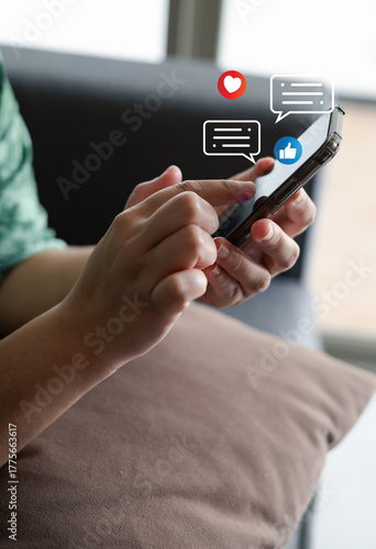 Close-up of a person using smartphone with social media icons, like, heart, and chat notification, representing online communication, social interaction, and digital connection in modern lifestyle.