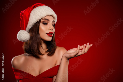 Beauty woman in Santa hat wearing an off shoulder red dress celebrating Christmas with glamorous makeup