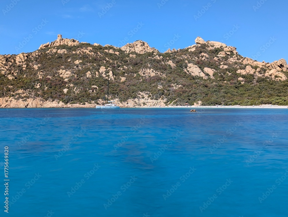 Fototapeta premium the bay of Roccapina with its beautiful smooth turquoise water seen from the sea, with the watchtower and reclining lion on the hill in the sunshine