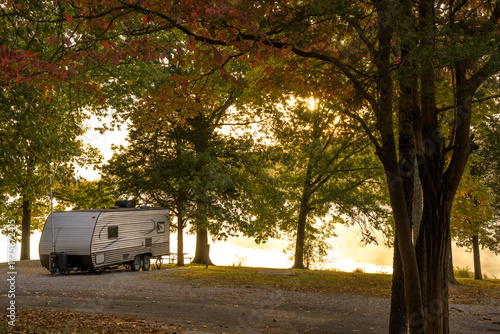 Fotografie Sunrise glows on a serene lake as an RV camper trailer rests peacefully in a vib