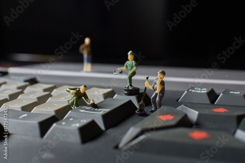 Miniature plastic workers pretending to fix an old computer keyboard against a black background