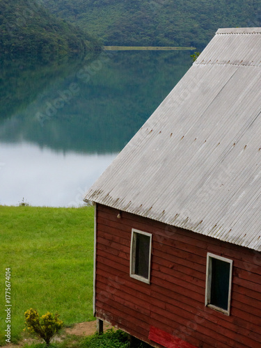 Rustic wooden cabin by tranquil lake surrounded by lush green hills in the early morning light